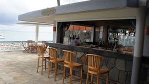 Un espace bar extérieur avec des chaises en bois et une vue sur la mer.