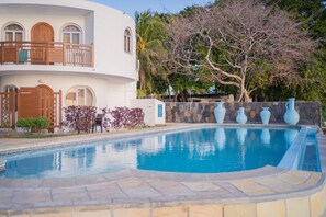 A swimming pool with a stone wall and vases, a white building with balconies, and a tree with bare branches. - Gold Beach Resort (Flic-en-Flac)
