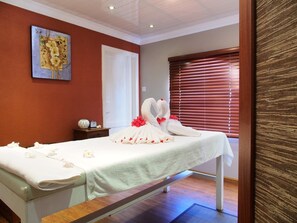A hotel room with a bed, a painting on the wall, a bedside table with a clock, and a window with blinds. - Gold Beach Resort (Flic-en-Flac)