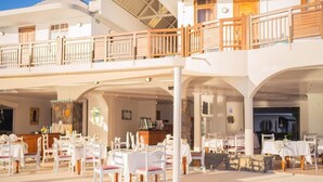 Un vaste espace extérieur aménagé pour les repas, avec plusieurs tables et chaises, un coin salon abrité et une balustrade en bois.