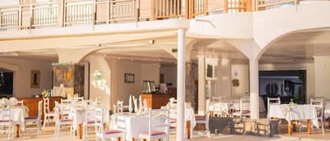 A spacious outdoor dining area with multiple tables and chairs, a covered seating area, and a wooden balcony railing.