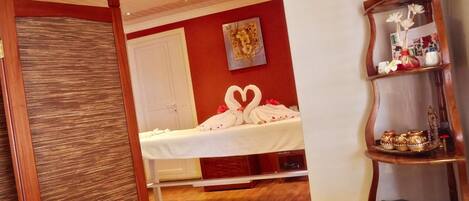 Una habitación de hotel con una cama, un estante de madera con adornos y una pared decorada con toallas dispuestas en forma de corazón.