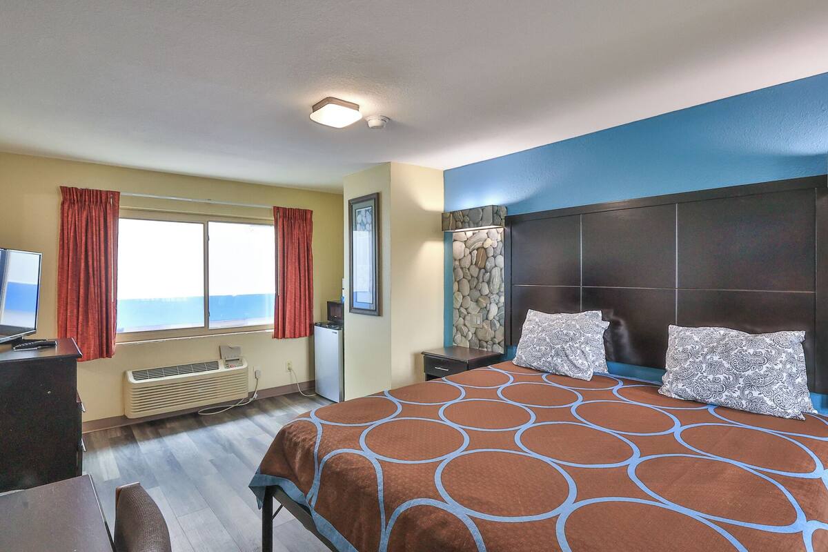 Una habitación de hotel con cama, escritorio, televisor y ventana con cortinas.