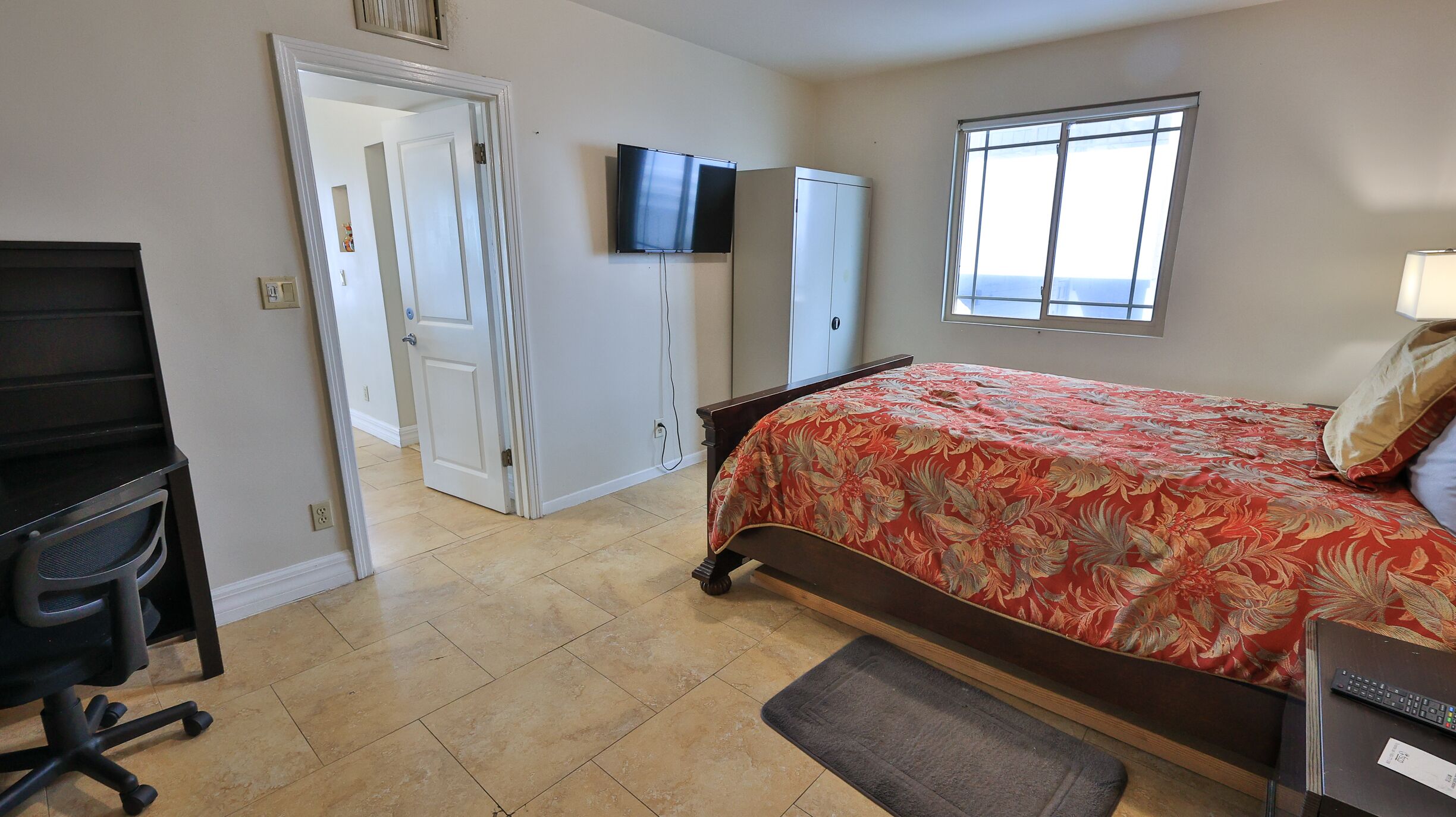 A bedroom with a bed, a desk, a chair, a wardrobe, a TV, and a window.