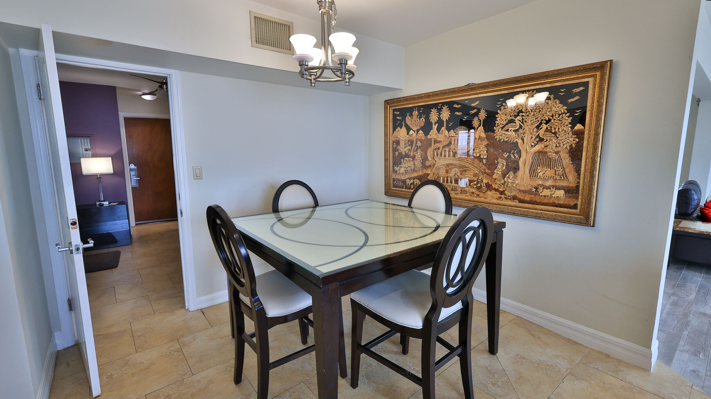 Un comedor con una mesa de vidrio, cuatro sillas y un cuadro decorativo grande en la pared.