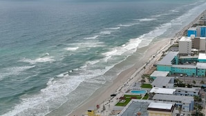 Vista aérea de una zona costera con una extensa playa, edificios y una piscina.
