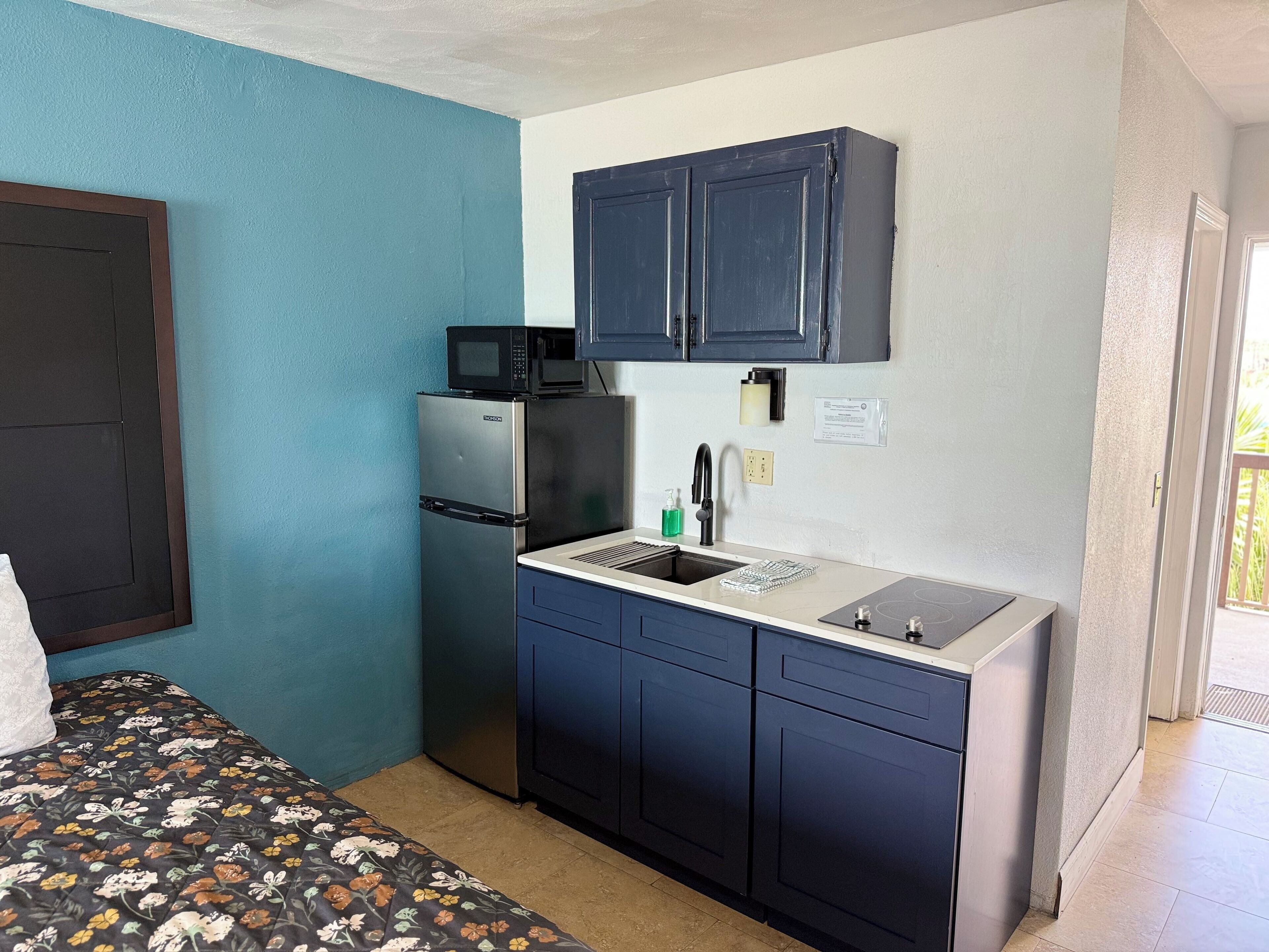 A compact kitchen with a refrigerator, microwave, sink, and blue cabinets.