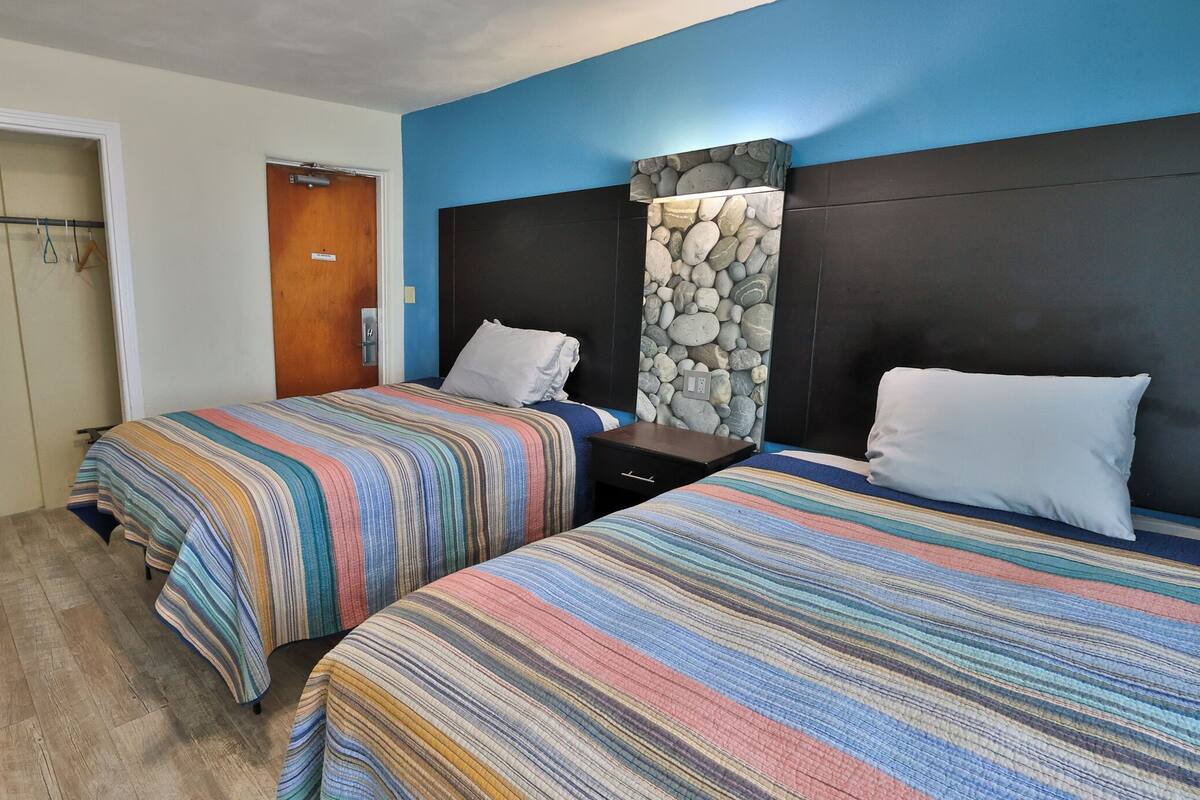 Habitación de hotel con dos camas, una puerta de madera, una pared decorativa de piedra y una mesita de noche pequeña.