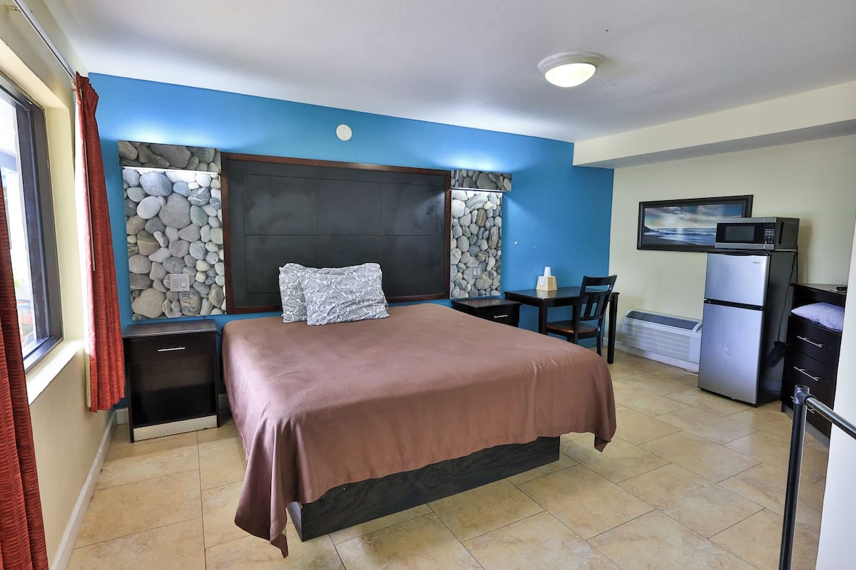 Habitación de hotel con cama, escritorio, silla, microondas, refrigerador y pared de piedra.