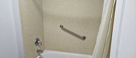 A bathroom with a bathtub, a shower curtain, and a grab bar.