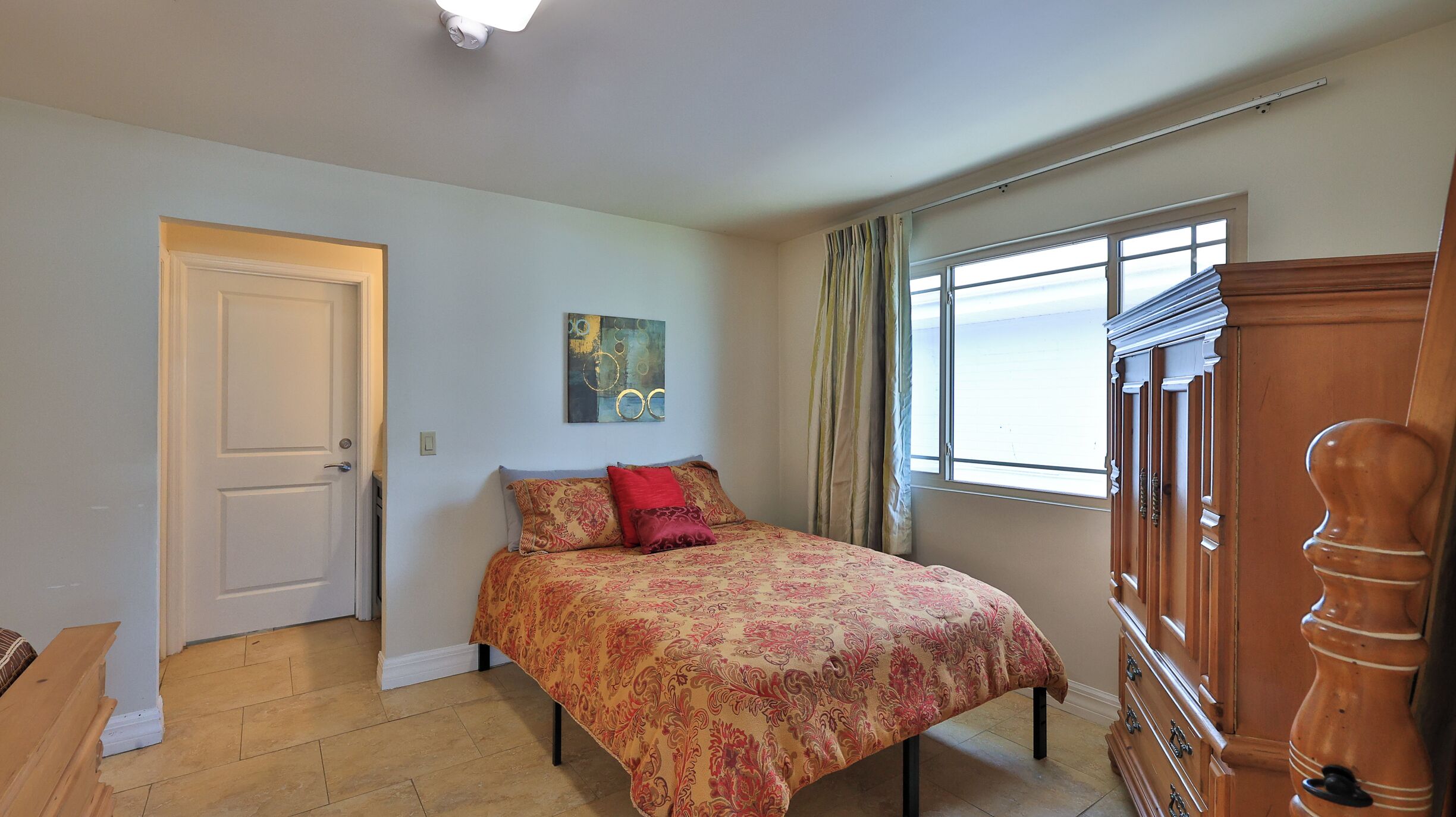 Un dormitorio con una cama, una ventana con cortinas, una puerta y un aparador de madera.