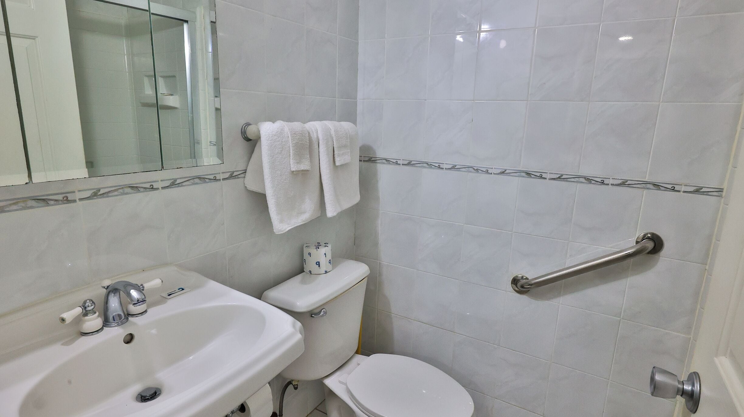 A bathroom with a sink, toilet, and handrail.