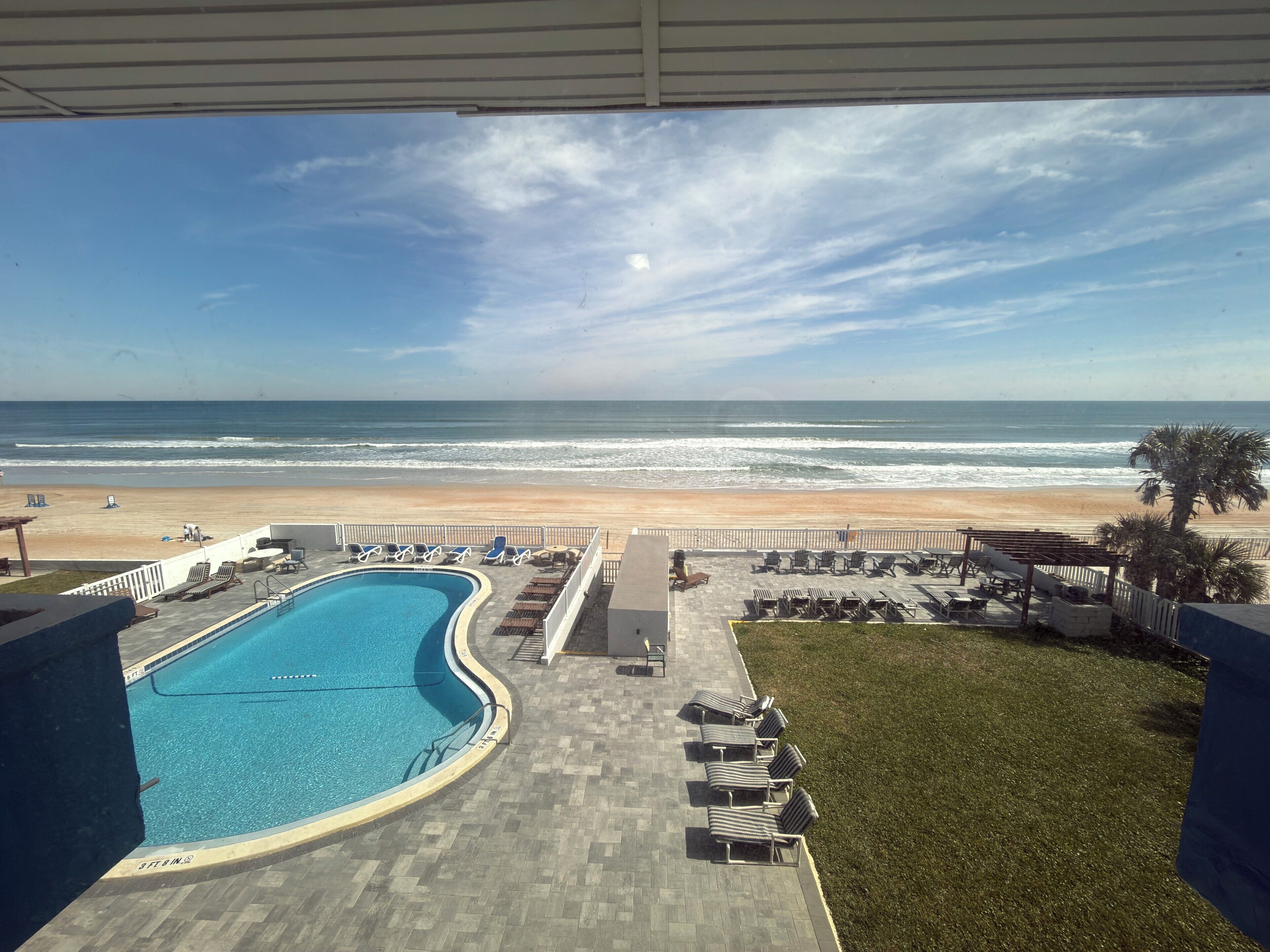 A pool with lounge chairs, a beach view, and a clear sky.
