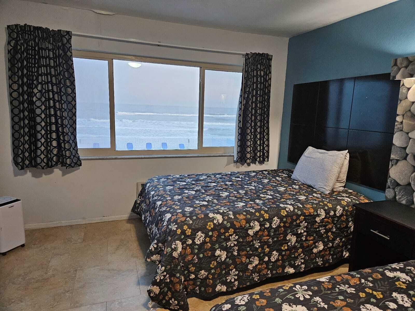 Un dormitorio con cama, cabecero, ventana con cortinas y pared de piedra.