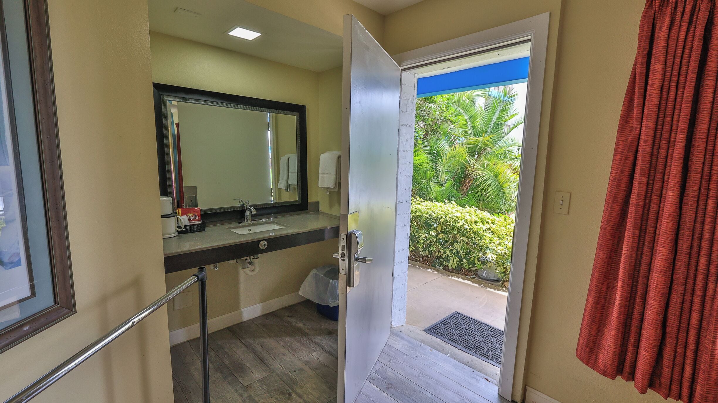 A bathroom with a sink, mirror, and a door leading to a balcony with a view of greenery.