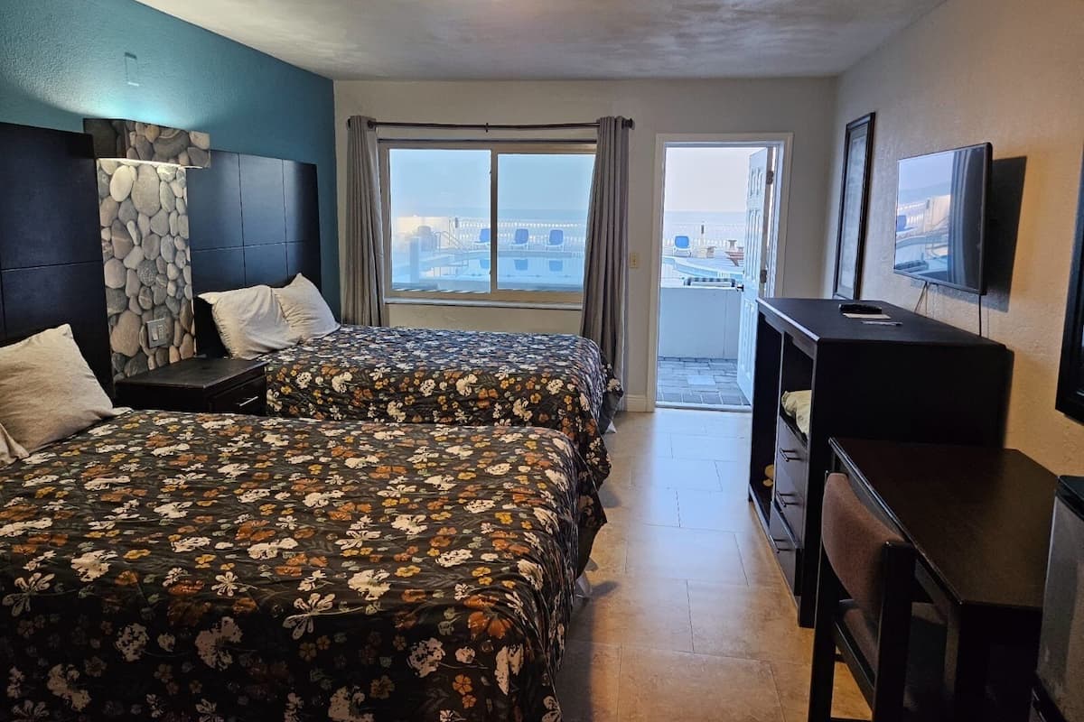 Habitación de hotel con dos camas, un escritorio, un televisor y un balcón con vista a la ciudad.