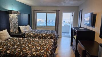 Een hotelkamer met twee bedden, een bureau, een televisie en een balkon met uitzicht over de stad.