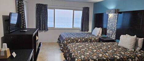 A hotel room with two beds, a desk with a computer, a window with curtains, and a stone wall decoration.