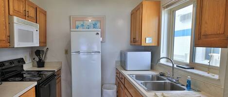 Una cocina funcional con gabinetes de madera, un refrigerador blanco, un microondas, una estufa y un lavamanos.