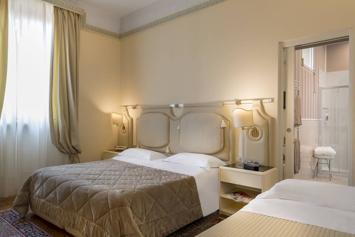 Ein Hotelzimmer mit einem großen Bett, Nachttischen, einem Nachtlicht und einem durch eine geöffnete Tür einsehbaren Badezimmer.