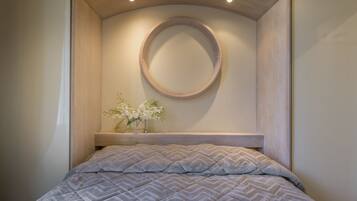 Un dormitorio con cama, un espejo redondo y un florero con flores.