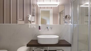 A modern bathroom with a white sink, a hairdryer, and a glass shower enclosure.