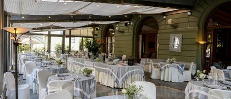 Un salón de banquetes con mesas redondas dispuestas para comer, con manteles blancos y sillas.