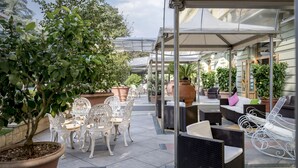 An outdoor patio area with white wicker furniture, potted plants, and a covered seating area. - Grand Hotel Tettuccio (Montecatini Terme)