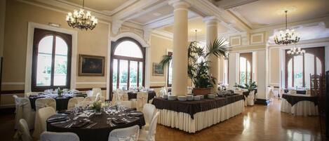 Une salle à manger élégante, avec des tables rondes, des chaises blanches, des lustres et de grandes fenêtres.