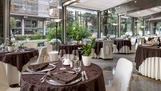 A restaurant with round tables, white chairs, and a view of the outdoors. - Grand Hotel Tettuccio (Montecatini Terme)