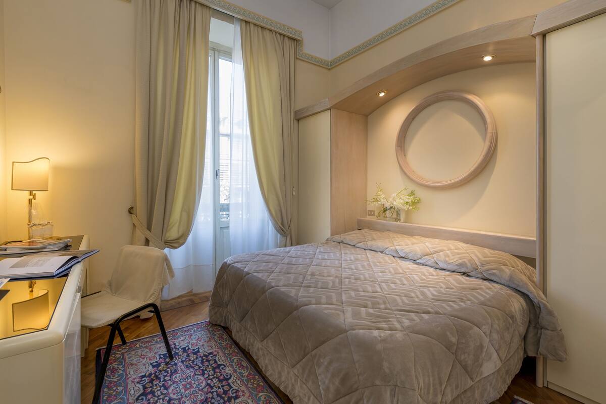 Ein Hotelzimmer mit einem Bett, einem Schreibtisch mit Lampe, einem Stuhl und einem Vorhangfenster.
