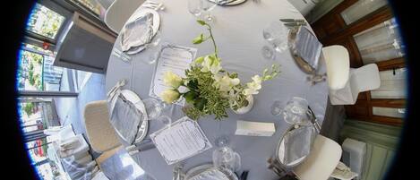 A round table set for a formal event with white tablecloths, silverware, and a floral centerpiece.