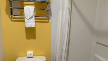 Un baño con una pared amarilla, un inodoro blanco, una cortina de ducha y un perchero con varias toallas.