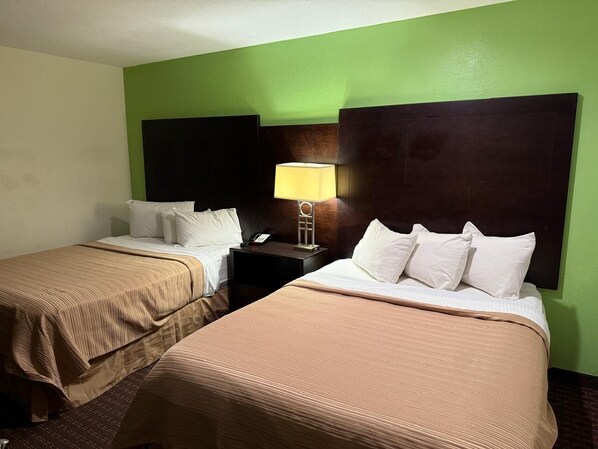 Habitación de hotel con dos camas, cada una con cabecera, mesita de noche y lámpara, y pared verde.