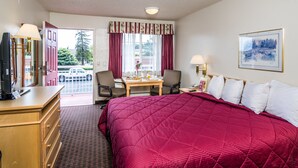 A hotel room with a large bed, a desk with a chair, a television, and a window with curtains. - Hollister Inn (Hollister)