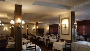 Een restaurant met meerdere tafels, elk gedekt met witte tafelkleden en voorzien van wijnglazen en bestek.
