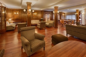Een ruime lobby met houten lambrisering, meerdere zithoeken met banken en fauteuils, en een eetgedeelte met houten tafels en stoelen.