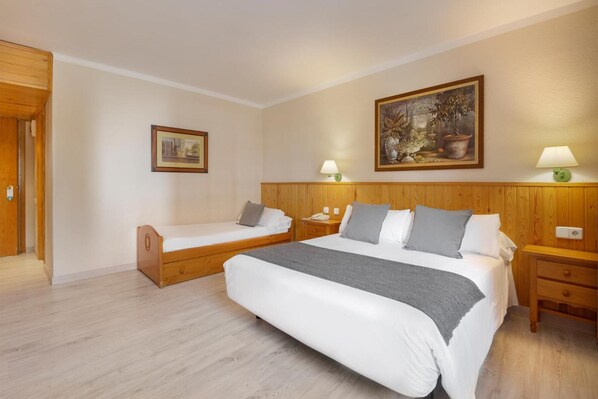 Habitación de hotel con una cama grande, dos camas más pequeñas, cabeceros de madera, un cuadro y lámparas de noche.