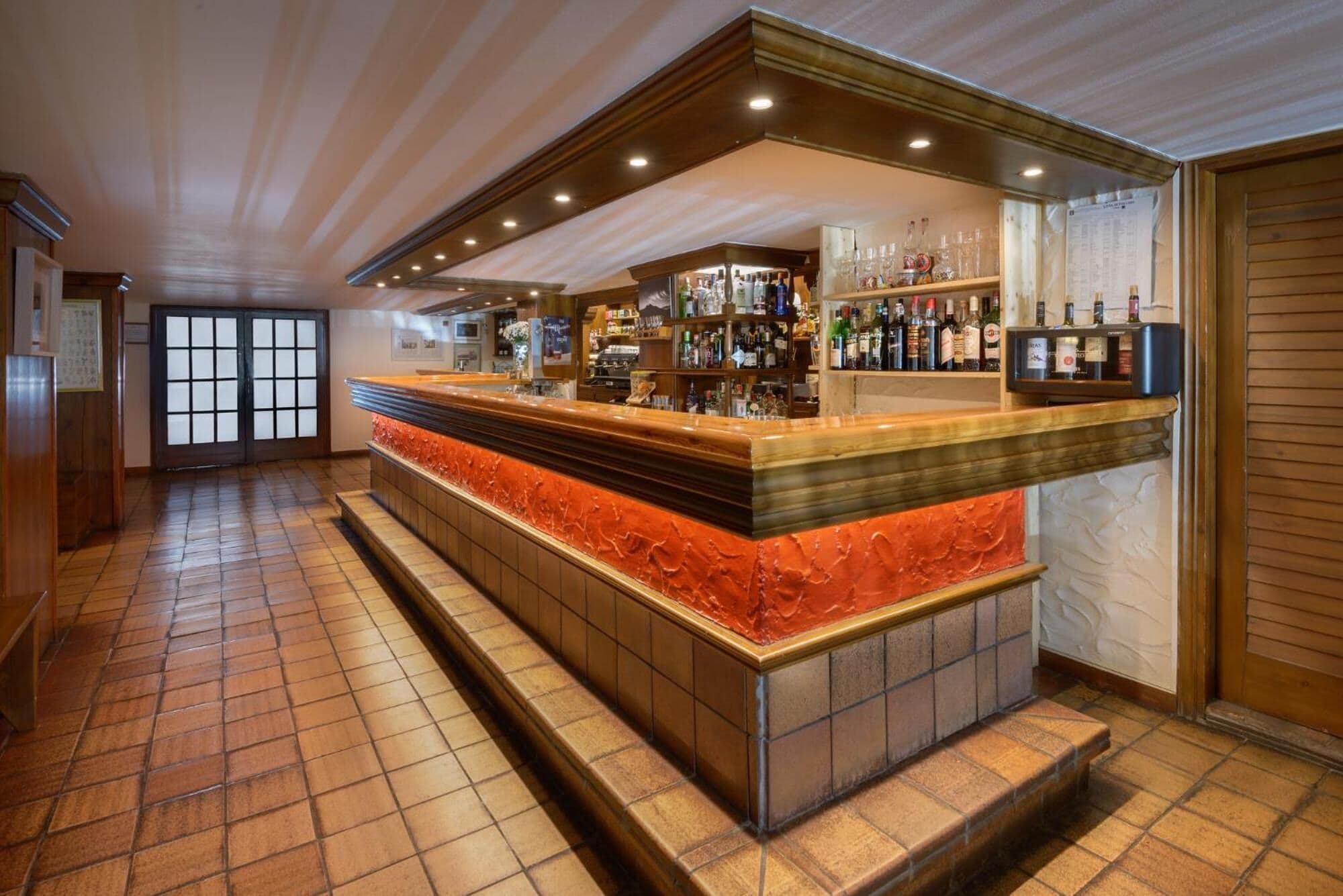 A bar area with a counter, shelves of bottles, and a tiled floor.
