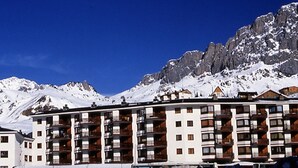 Een hotel met meerdere verdiepingen en balkons, gelegen voor een besneeuwde berg.