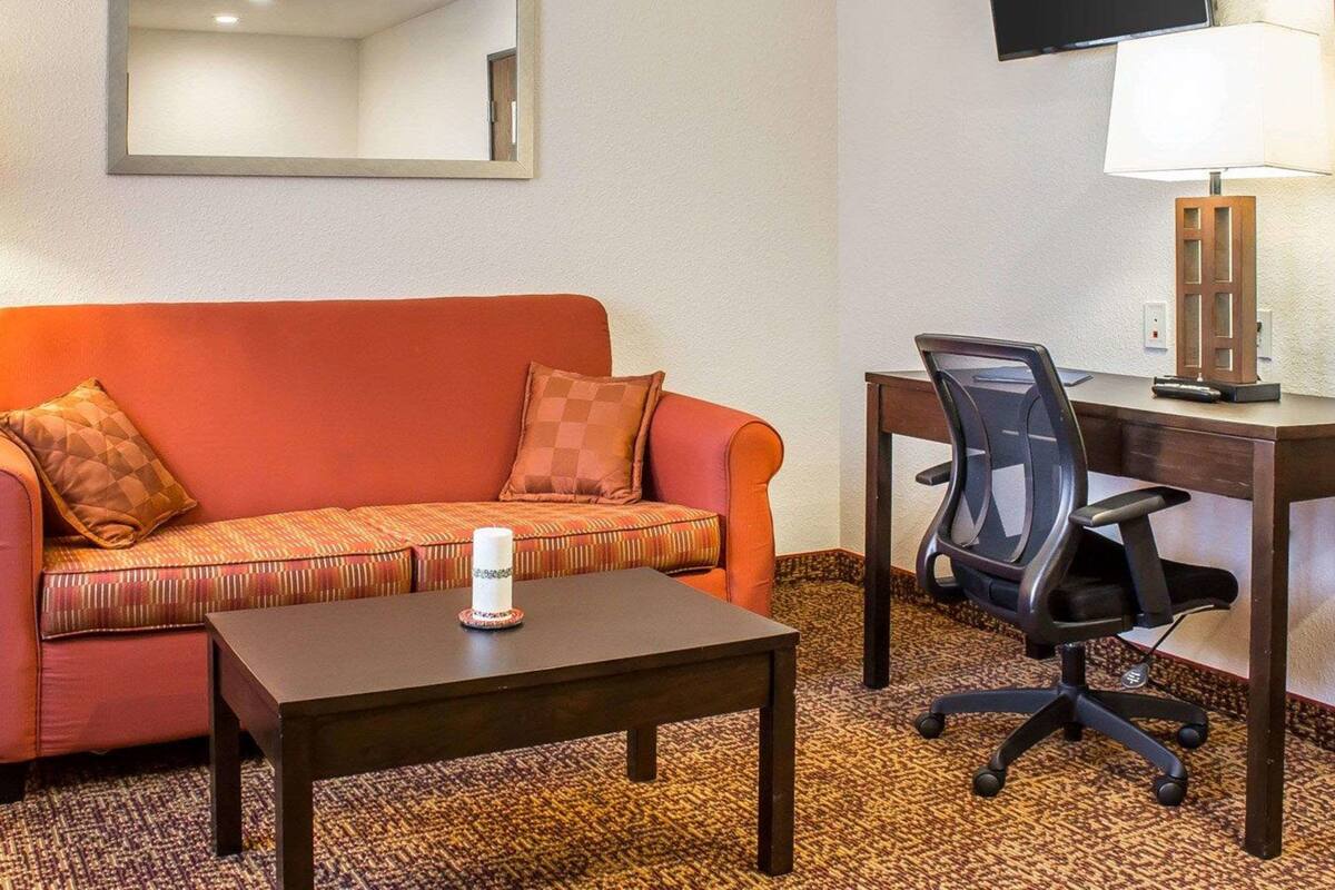 A hotel room with a sofa, a small table with a candle, a desk with a chair, a TV, and a lamp.
