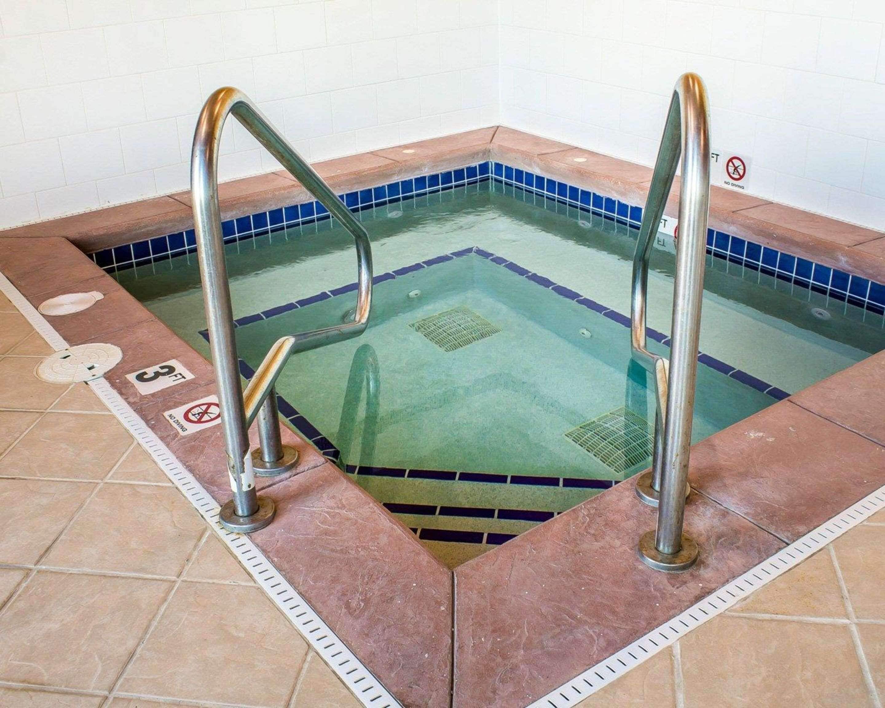 Une piscine équipée de deux échelles métalliques, d’une bordure carrelée bleue et d’un panneau indiquant « Interdiction de plonger ».
