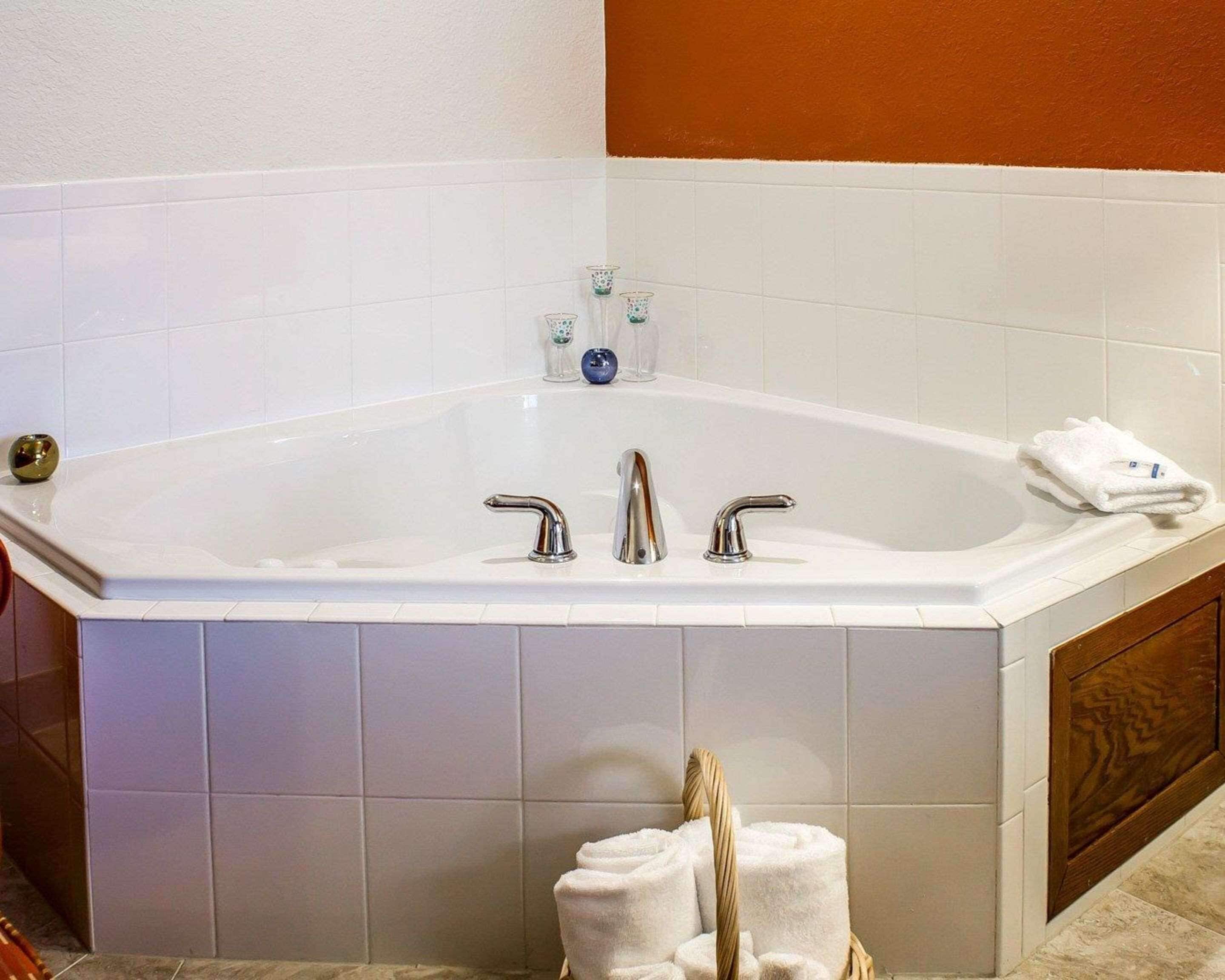 A large bathtub with two faucets, a glass of water, and a towel on the side.