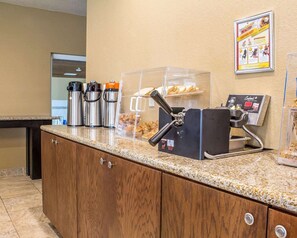 A breakfast bar with coffee makers, a toaster, and a display case with pastries.