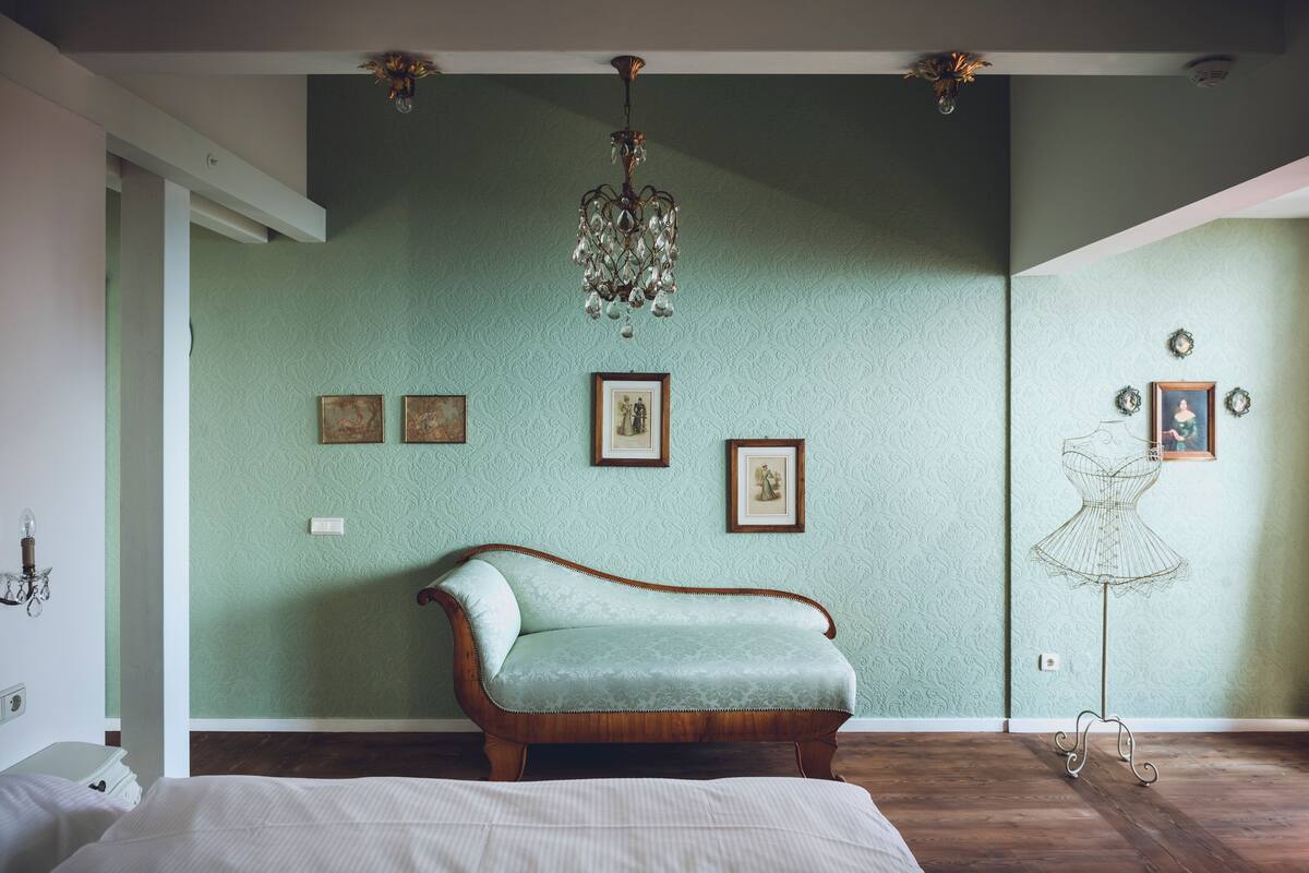 A room with a green textured wall, a wooden sofa, a standing lamp, and a mannequin on a stand.