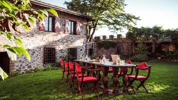 A stone building with a garden patio, red chairs, and a table set for dining.