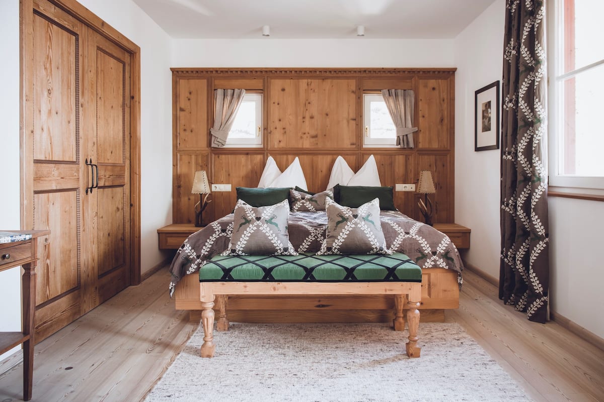 A wooden bed with a green and white patterned bedspread, flanked by two nightstands with lamps, in a room with wooden paneling and a large wardrobe.