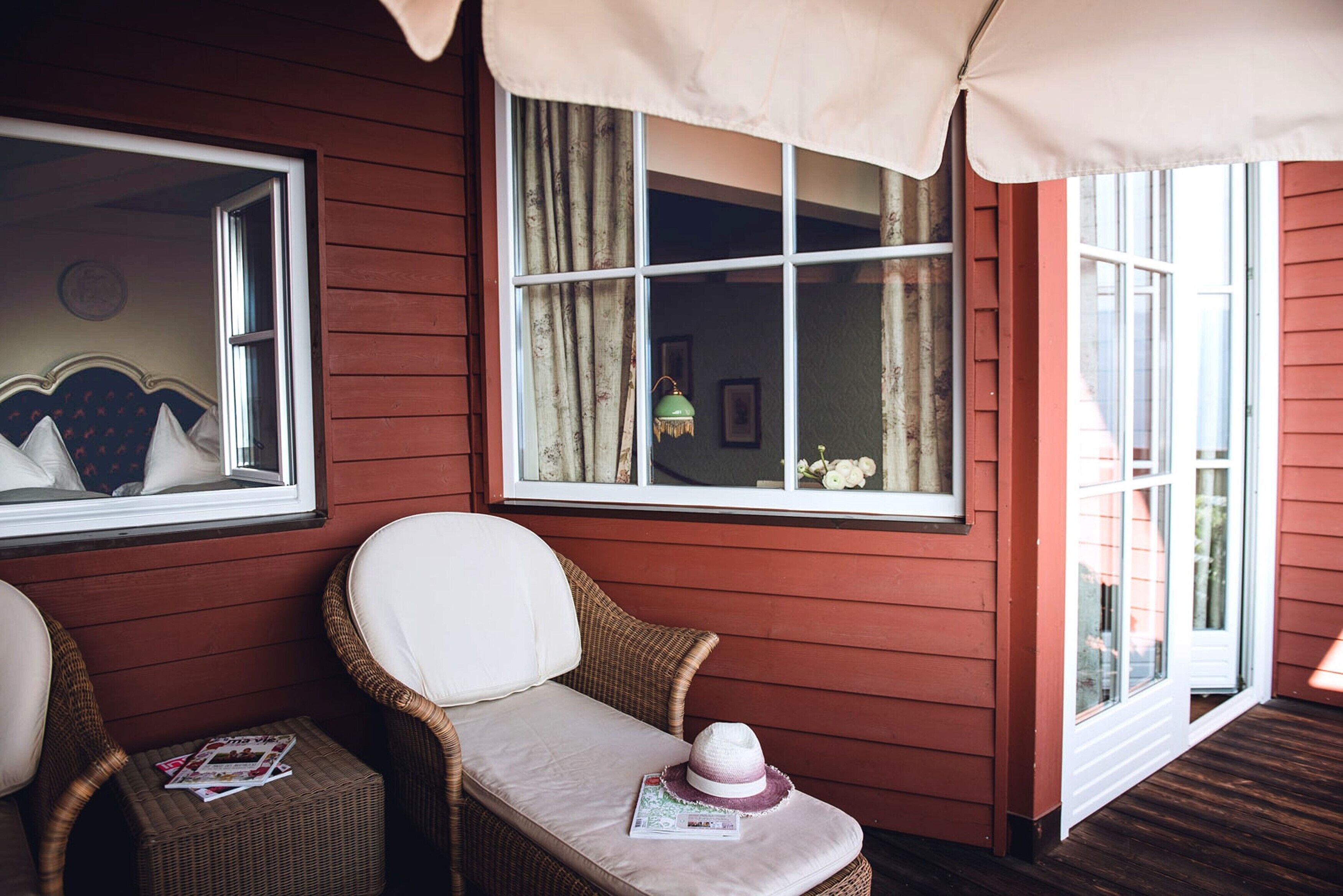 A cozy room with wicker chairs, a cushioned bench, and a window with curtains.