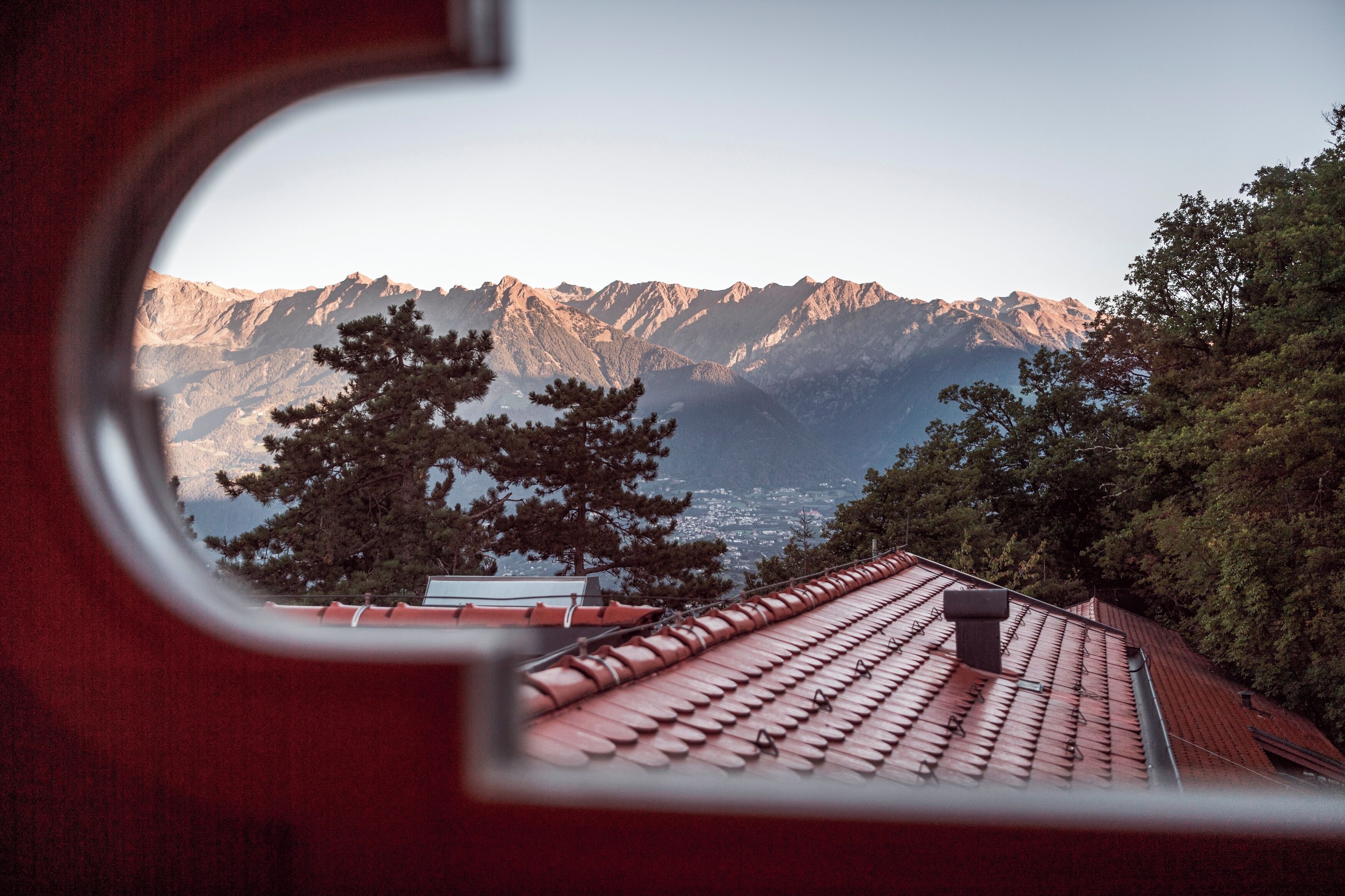 Paisaje montañoso visto a través de una ventana con tejado de tejas rojas.