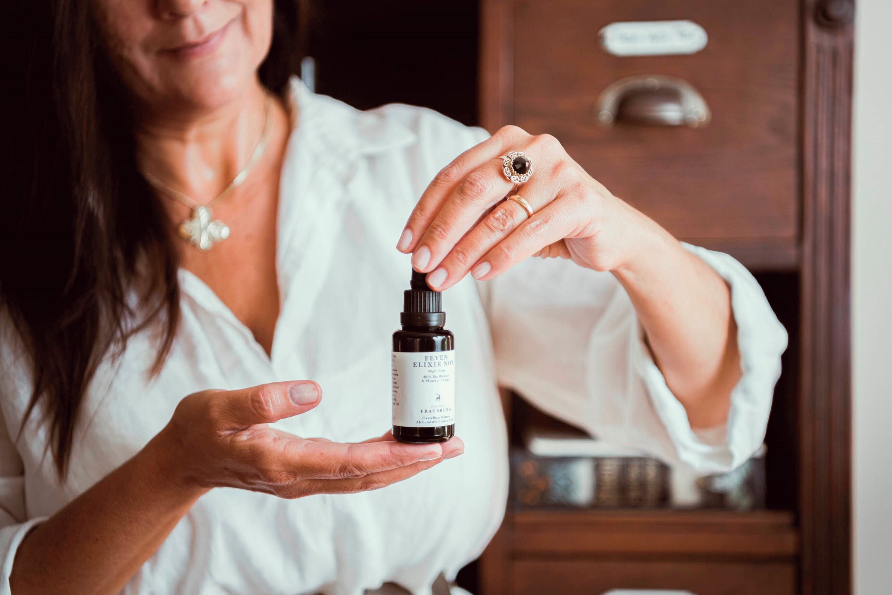 A person holding a small bottle with a label.